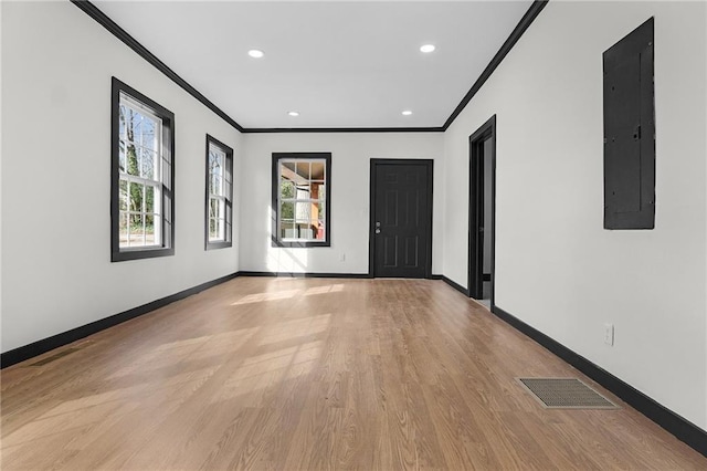 empty room featuring visible vents, baseboards, light wood-type flooring, electric panel, and crown molding