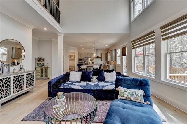 living room with decorative columns, crown molding, a towering ceiling, and light hardwood / wood-style floors