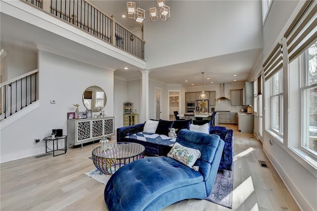 living room with a towering ceiling, ornamental molding, light hardwood / wood-style flooring, and ornate columns