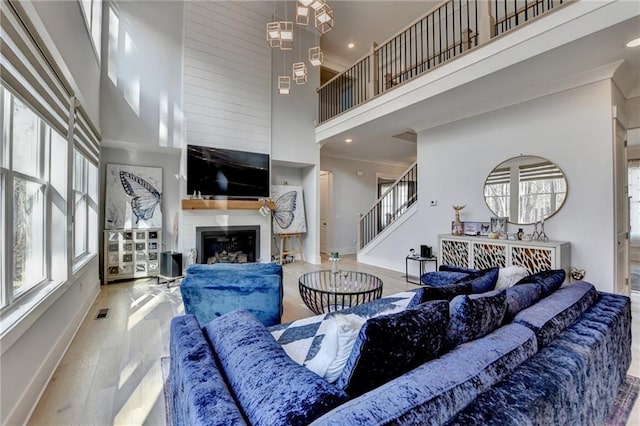 living room with hardwood / wood-style floors, a towering ceiling, ornamental molding, and a large fireplace