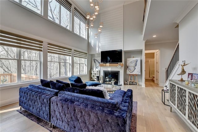 living room with a high ceiling, crown molding, a chandelier, and light wood-type flooring