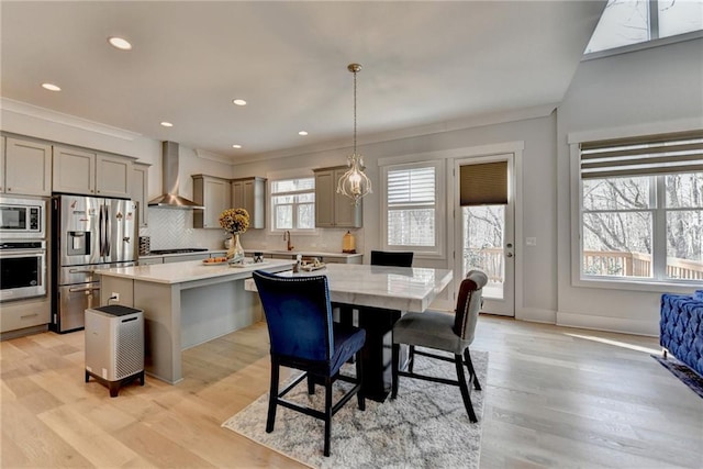 kitchen featuring wall chimney exhaust hood, a center island, appliances with stainless steel finishes, pendant lighting, and backsplash