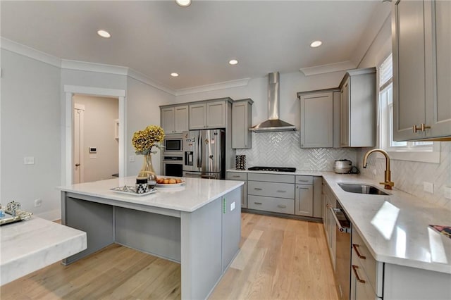 kitchen with sink, a center island, appliances with stainless steel finishes, gray cabinets, and wall chimney range hood