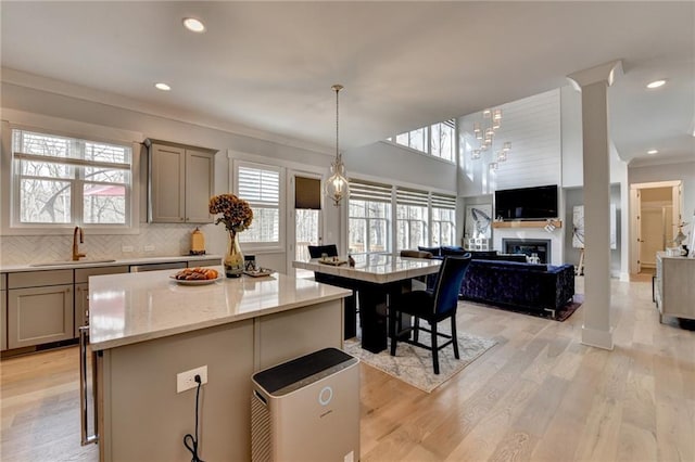 kitchen with gray cabinetry, hanging light fixtures, a kitchen island, light stone counters, and a kitchen bar