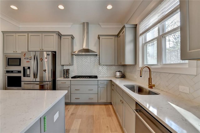 kitchen with stainless steel appliances, light stone countertops, sink, and wall chimney range hood