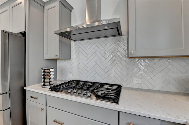 kitchen with wall chimney range hood, gray cabinets, appliances with stainless steel finishes, light stone counters, and decorative backsplash