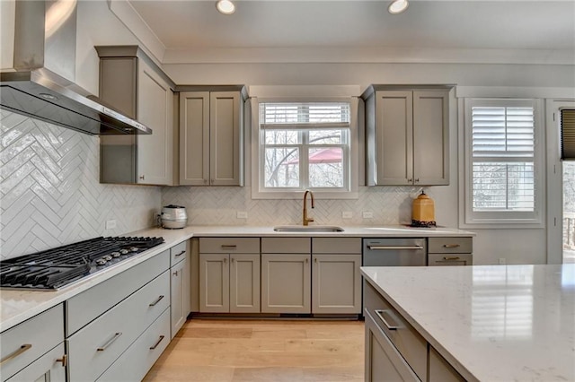 kitchen with stainless steel gas stovetop, light stone countertops, sink, and wall chimney range hood