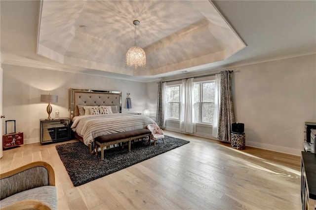 bedroom featuring ornamental molding, a tray ceiling, light hardwood / wood-style flooring, and a notable chandelier