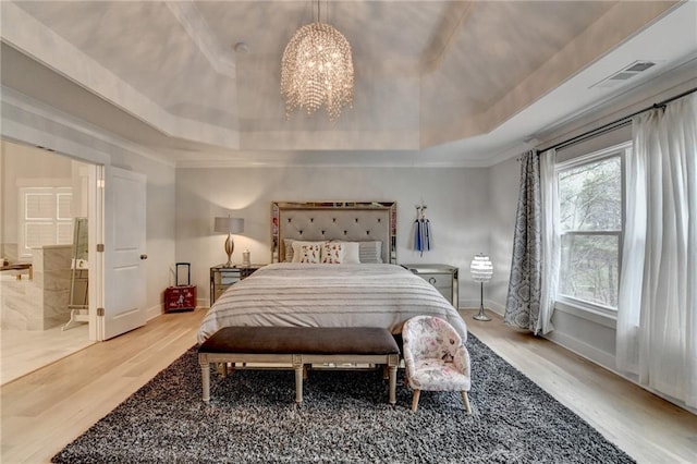 bedroom featuring a raised ceiling, hardwood / wood-style flooring, a chandelier, and ensuite bath