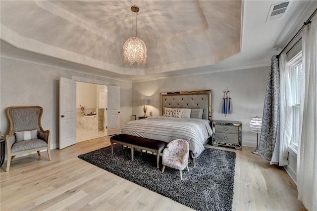 bedroom with an inviting chandelier, light hardwood / wood-style flooring, ensuite bath, and a tray ceiling