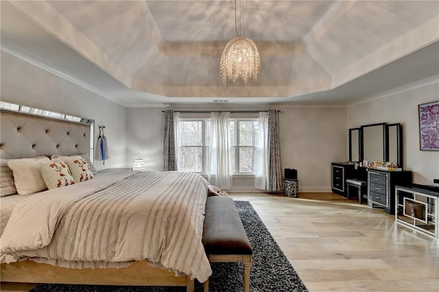 bedroom with crown molding, an inviting chandelier, light wood-type flooring, and a tray ceiling