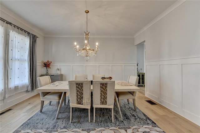 dining area with ornamental molding, an inviting chandelier, and light hardwood / wood-style flooring