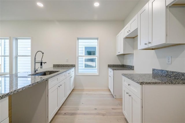 kitchen featuring recessed lighting, light stone countertops, light wood-style floors, and a sink