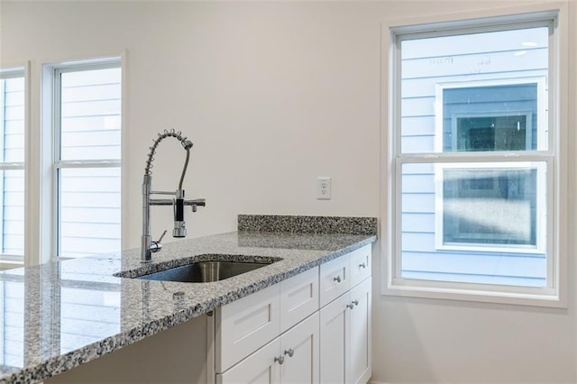 kitchen featuring white cabinets, light stone countertops, and a sink