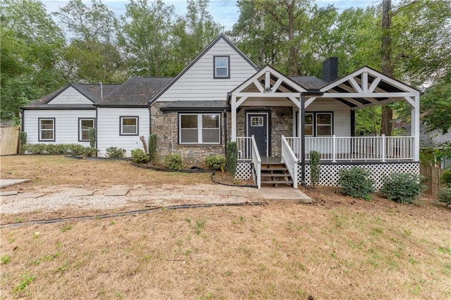 view of front of house with stone siding, a front yard, a porch, and a chimney