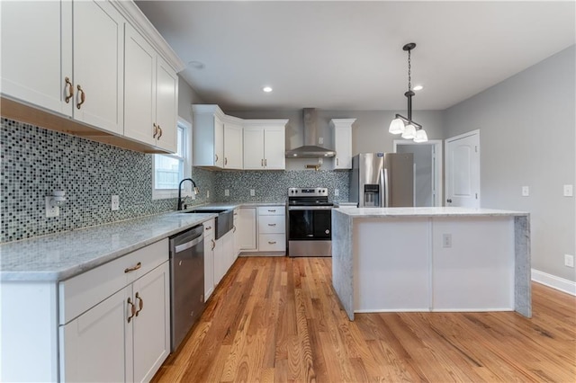 kitchen with decorative light fixtures, appliances with stainless steel finishes, a kitchen island, wall chimney range hood, and white cabinets