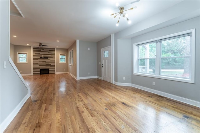 unfurnished living room with ceiling fan with notable chandelier, a fireplace, and light wood-type flooring