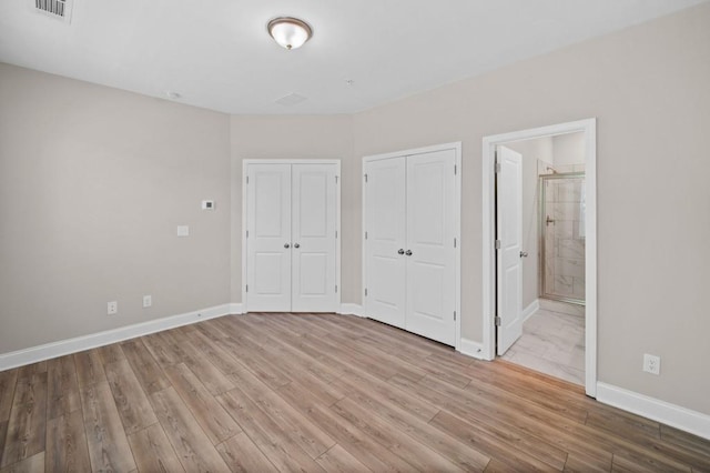 unfurnished bedroom with wood finished floors, baseboards, two closets, and ensuite bathroom