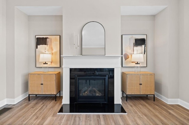 detailed view of wood finished floors, baseboards, and a glass covered fireplace