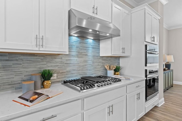 kitchen featuring under cabinet range hood, crown molding, stainless steel appliances, decorative backsplash, and white cabinets