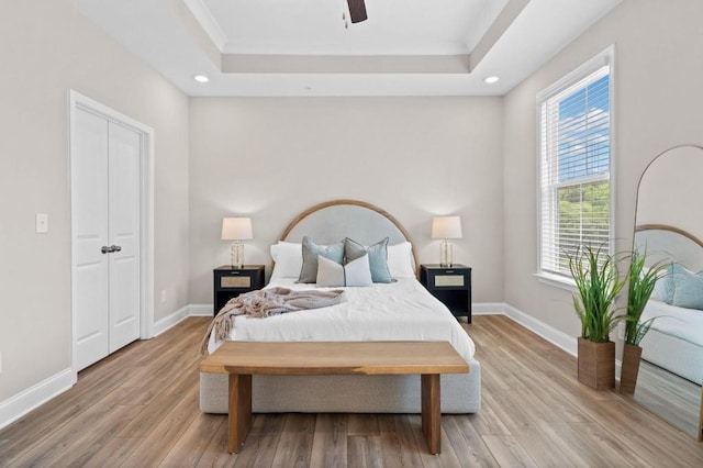 bedroom with a raised ceiling, wood finished floors, ornamental molding, recessed lighting, and baseboards
