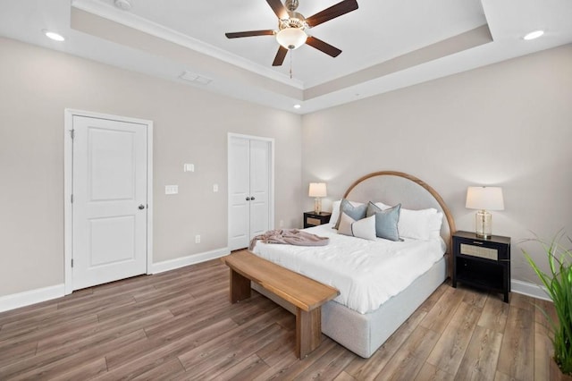 bedroom featuring a raised ceiling, baseboards, light wood finished floors, recessed lighting, and crown molding