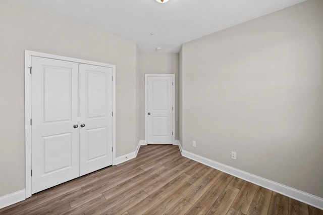 unfurnished bedroom featuring baseboards, wood finished floors, and a closet
