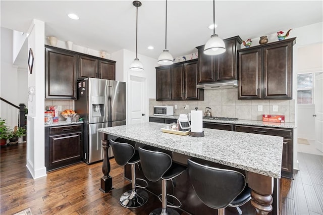 kitchen with a center island, backsplash, pendant lighting, dark brown cabinets, and appliances with stainless steel finishes