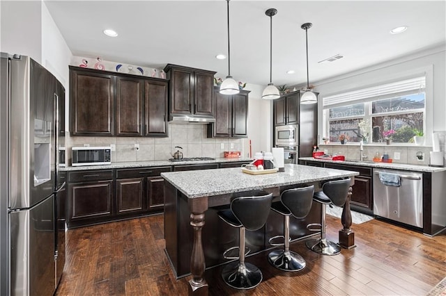 kitchen featuring backsplash, dark brown cabinetry, stainless steel appliances, decorative light fixtures, and a kitchen island