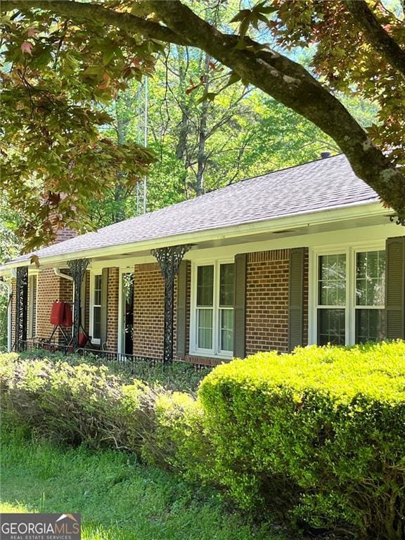 view of front of house featuring covered porch, a shingled roof, and brick siding