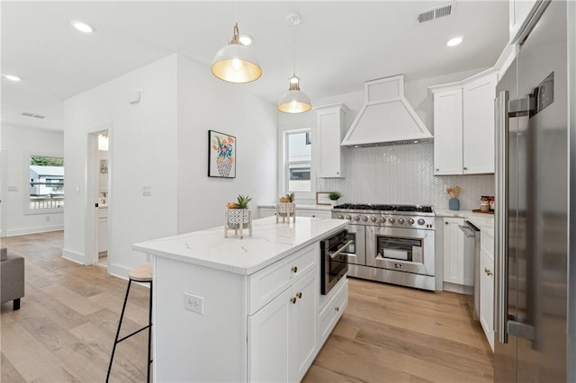 kitchen with visible vents, backsplash, light wood-style floors, high quality appliances, and premium range hood