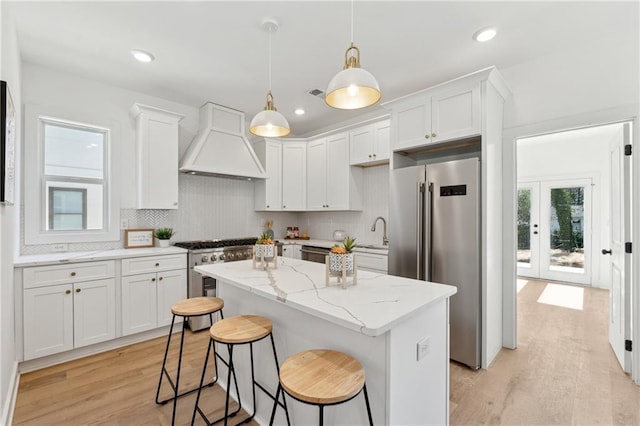 kitchen with white cabinetry, premium range hood, a kitchen island, and appliances with stainless steel finishes