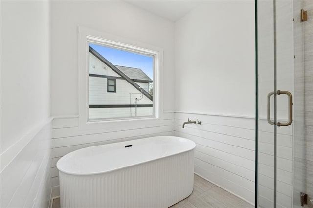 bathroom with a wainscoted wall, a freestanding tub, and a shower stall