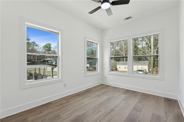 unfurnished room featuring a ceiling fan, baseboards, visible vents, and wood finished floors