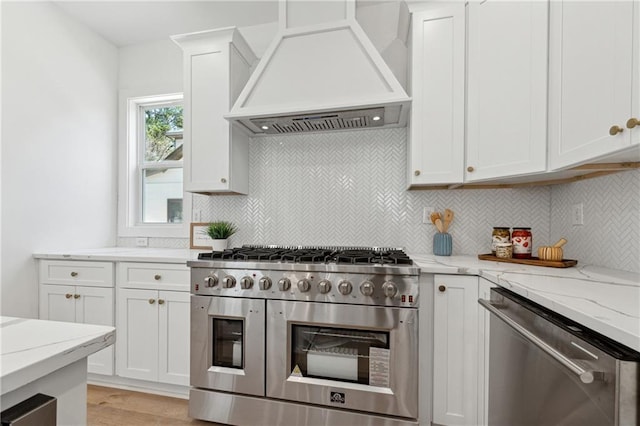 kitchen featuring appliances with stainless steel finishes, custom range hood, backsplash, and white cabinetry