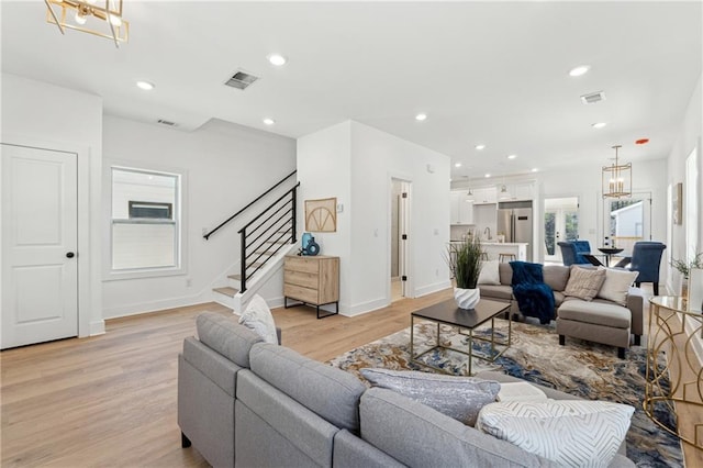 living area with a chandelier, light wood finished floors, stairs, and recessed lighting