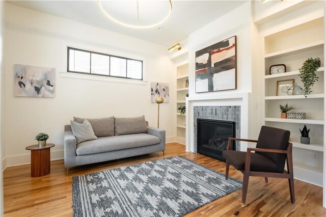 living area with a tile fireplace, wood-type flooring, and built in shelves