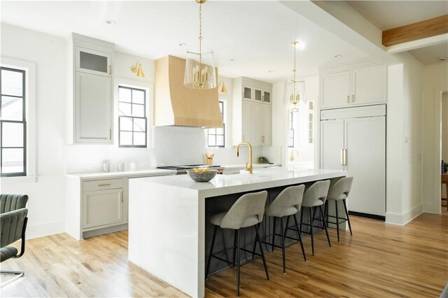 kitchen with a center island with sink, light hardwood / wood-style floors, beam ceiling, and paneled fridge