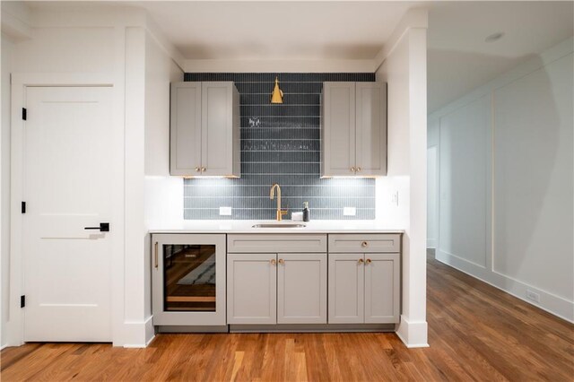 bar featuring gray cabinetry, beverage cooler, light hardwood / wood-style flooring, and sink