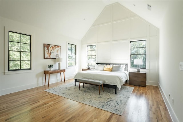 bedroom featuring high vaulted ceiling, multiple windows, and hardwood / wood-style flooring