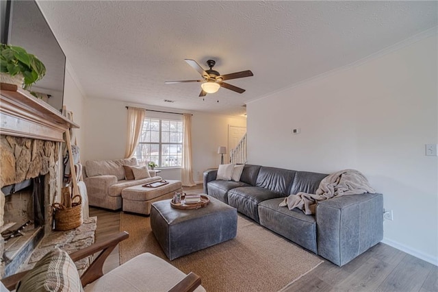 living room with ceiling fan, a stone fireplace, wood-type flooring, and a textured ceiling