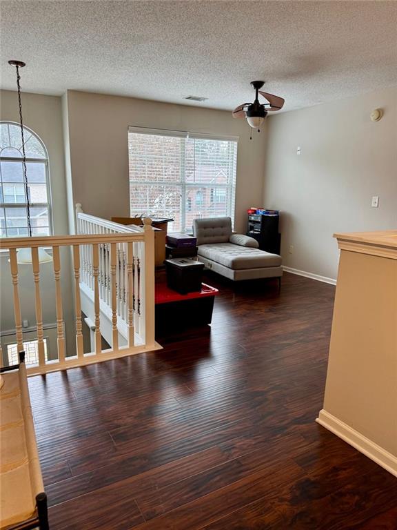 living room featuring a textured ceiling, ceiling fan, and dark wood-type flooring