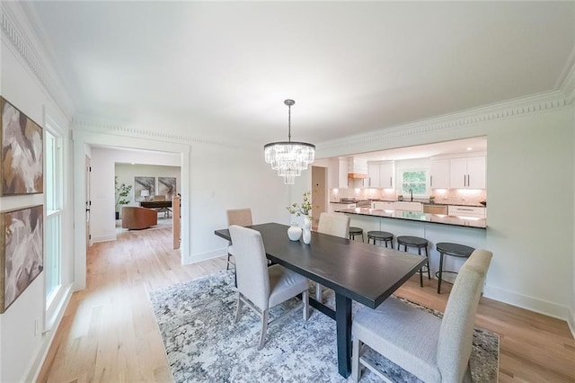 dining space with crown molding, sink, an inviting chandelier, and light hardwood / wood-style flooring