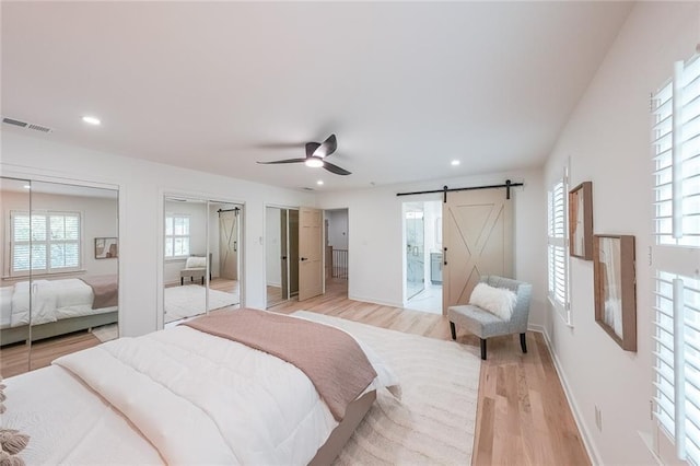 bedroom featuring ceiling fan, multiple closets, light wood-type flooring, and a barn door