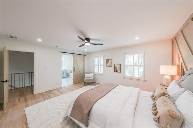 bedroom with ensuite bath, ceiling fan, a barn door, and light hardwood / wood-style floors