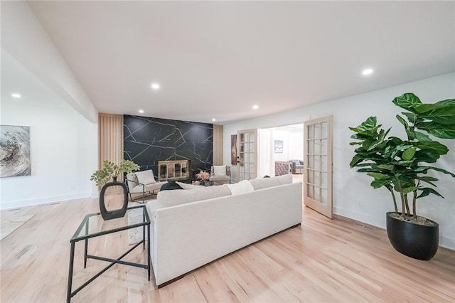 living room with french doors, light wood-type flooring, and a high end fireplace