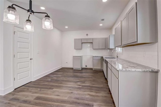 kitchen with dark wood-type flooring, sink, gray cabinetry, backsplash, and light stone countertops