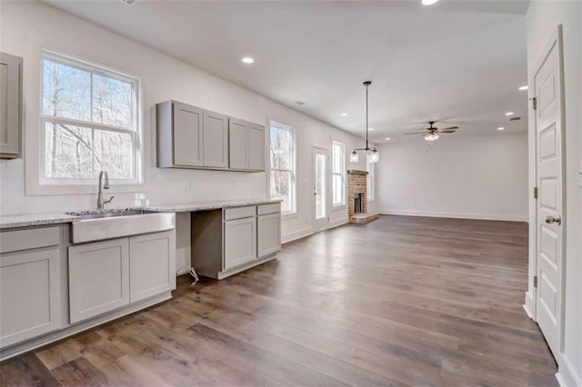 kitchen featuring dark wood-type flooring, gray cabinetry, a brick fireplace, decorative light fixtures, and ceiling fan