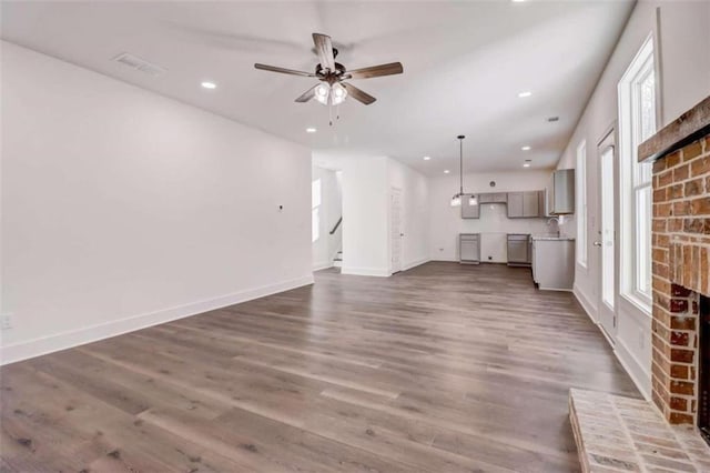 unfurnished living room with ceiling fan, sink, a fireplace, and dark hardwood / wood-style flooring