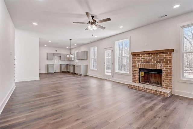 unfurnished living room with a healthy amount of sunlight, ceiling fan, a fireplace, and dark hardwood / wood-style flooring